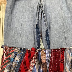 Pode incluir: Uma saia de ganga com uma fenda nas costas, apresentando uma camada inferior de tiras de tecido coloridas costuradas juntas. As tiras de tecido s&atilde;o feitas de v&aacute;rias gravatas estampadas.