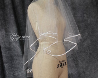 May include: White bridal veil with a single layer of tulle and a white satin ribbon trim. The veil is displayed on a mannequin.