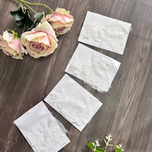 May include: Four samples of white lace fabric on white cards, labeled "White", "Off-white", and "Light Ivory". The lace has intricate floral patterns. The image also includes pink roses and greenery, all arranged on a wooden surface.