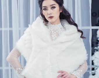May include: A white faux fur shawl with a long, flowing design. The shawl is worn over a white lace dress. The model is standing in front of a white background.