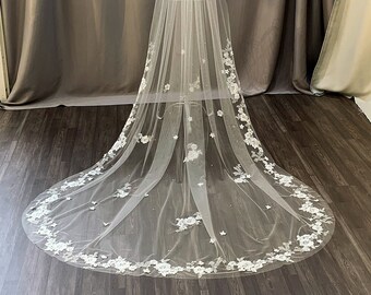 May include: A long, white bridal veil with a delicate floral lace trim. The veil is made of soft tulle and features a scattering of small pearls.