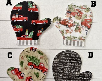 Op de afbeelding: Vier verschillende kerst-ovenwantjes. De wantjes zijn gevormd als wanten en hebben een gestreepte manchet. De wantjes hebben verschillende ontwerpen, waaronder een rode vrachtwagen met een kerstboom, een winterscène met een rode vrachtwagen, een rode vrachtwagen met een kerstboom op een beige achtergrond en een zwart-wit ontwerp met de woorden "Vallende sneeuw", "Thuis blijven", "Warme open haard", "Oud-Hollands", "Sleigh Rides", "Sneeuwvlokken" en "Warme chocolademelk".