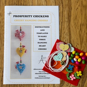 May include: A craft kit for making three hanging heart-shaped decorations. The kit includes instructions, templates, felt, buttons, beads, and string. The instructions include the text "Prosperity Chickens Cheery Hanging Chooks".