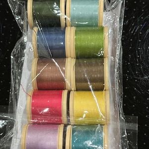 May include: A set of ten spools of thread in various colours, including green, blue, brown, red, yellow, purple, and teal. The spools are wrapped in clear plastic and have wooden bobbins.