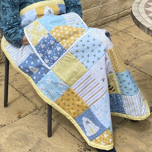 May include: A patchwork quilt in yellow, blue and white colours. The quilt features a bee and flower design.