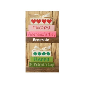 May include: Stackable wooden blocks with a reversible design. One side says "Happy Valentine's Day" with red hearts and the other side says "Happy St. Patrick's Day" with green shamrocks.