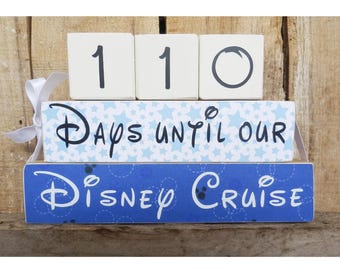 May include: White wooden blocks with the numbers 110 stacked on top of each other. The blocks are on top of a blue and white block with the text "Days until our Disney Cruise".