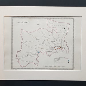 May include: A framed map of Middlesex, England, with a detailed layout of the area. The map features a red border, various place names, and a compass rose. The map is in a white mat.