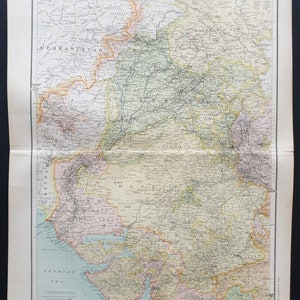 May include: A detailed vintage map of India, printed on aged paper. The map features a colour palette of beige, green, and pink, with the title "INDIA" at the top. It shows the borders of Afghanistan and the Arabian Sea, with place names.