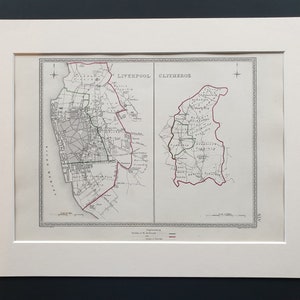 May include: Framed vintage map print featuring detailed cartography of Liverpool and Clitheroe, England. The map is in black and white with red and green border lines. The print is set in a white mat.