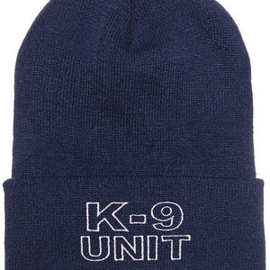 May include: A navy blue knit beanie with a white embroidered design that says "K-9 UNIT".