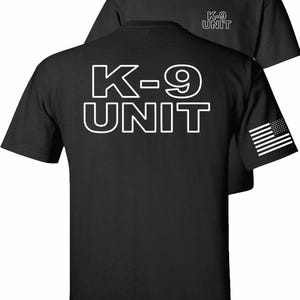 May include: A black short-sleeve t-shirt featuring the text K-9 UNIT in large white outlined letters on the back and smaller white text on the front chest. A white American flag graphic is printed on the left sleeve of the garment.