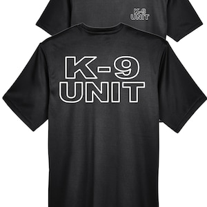 May include: Two black t-shirts. The front shirt displays the text "K-9 UNIT" in large white block letters. The second shirt, in the background, has the text "K-9 UNIT" in smaller white letters. Both shirts have short sleeves and a crew neck.
