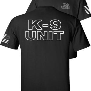 May include: Black t-shirts with white text and graphics. The front shirt displays "K-9 UNIT" in large block letters. The back of the shirt has the same text. The left sleeve has a small American flag graphic, and the right sleeve has white stripes.