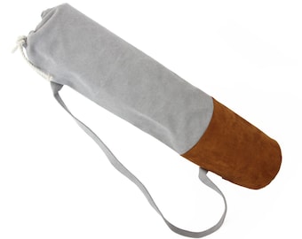 Könnte beinhalten: Eine graue Yogamatte-Tasche mit braunem Wildlederboden und Kordelzug. Die Tasche hat einen langen Trageriemen.