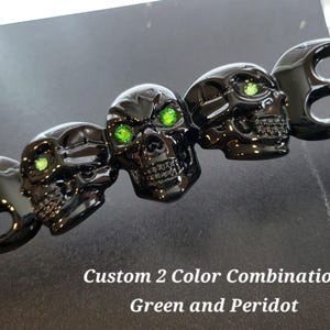 May include: A black decorative piece featuring three skull heads with green gem eyes. The text "Custom 2 Color Combination Green and Peridot" is displayed below the skulls.
