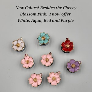 May include: Eight flower-shaped charms in white, aqua, red, purple, and cherry blossom pink. Each charm features five petals, a gold-toned center, and a small crystal accent. Text reads: New Colors! Besides the Cherry Blossom Pink, I now offer White, Aqua, Red and Purple.