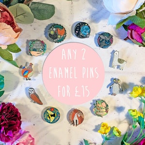 May include: A selection of enamel pins with various designs, including a chicken, owl, bee, fox, penguin, llama, and a globe. The pins are arranged on a white surface with flowers and greenery. The text "ANY 2 ENAMEL PINS FOR £15" is written on a pink circle.