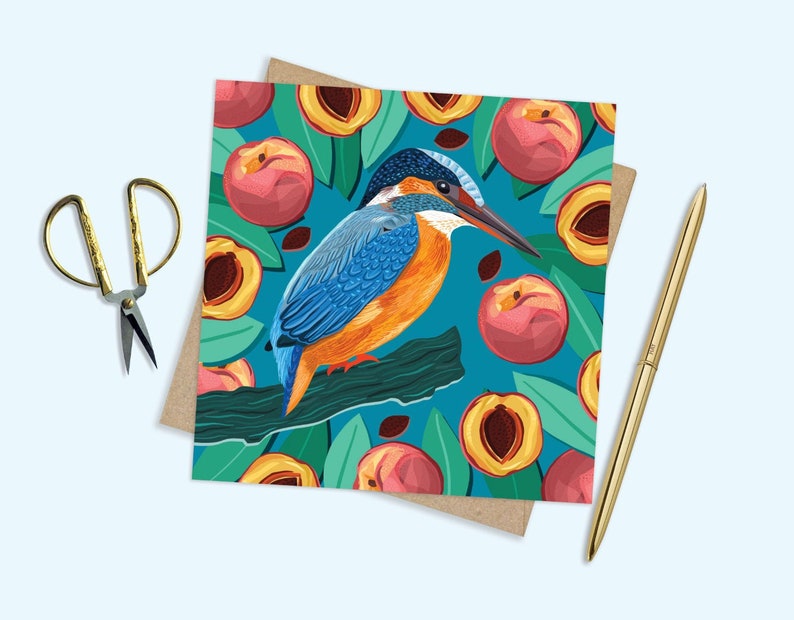 May include: A colorful greeting card featuring a blue and orange kingfisher bird perched on a branch with a background of peach fruit and green leaves.