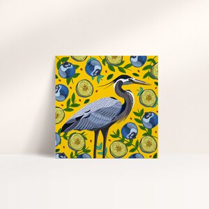 May include: A blue heron stands on a yellow background with a pattern of blueberries and lime slices. The heron has a long neck and beak, and its feathers are a mix of gray and blue.