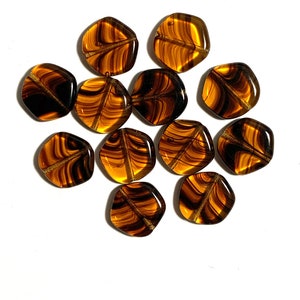 May include: A collection of 12 brown and gold glass beads with a swirled pattern. The beads are shaped like irregular hexagons.