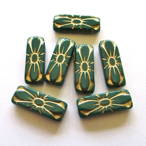 May include: Eight green glass beads with gold flower designs. The beads are rectangular in shape and have a glossy finish.