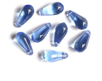 May include: A group of eight light blue glass teardrop beads. The beads are smooth and shiny, and they have a slightly iridescent finish.