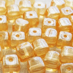 May include: A pile of iridescent gold square glass beads. The beads have a slightly frosted finish and are perfect for jewelry making.