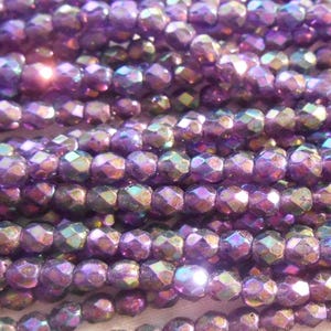 May include: A strand of iridescent purple faceted glass beads. The beads are small and have a shiny, reflective finish.