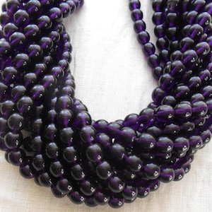 May include: A strand of deep purple glass beads. The beads are round and have a smooth, glossy finish.