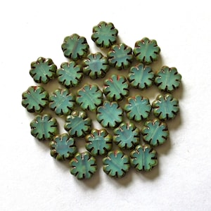 May include: A collection of flower-shaped beads in shades of teal and green. The beads have a scalloped edge and a translucent appearance, with a hint of red at the center. These beads are ideal for jewelry making and craft projects.