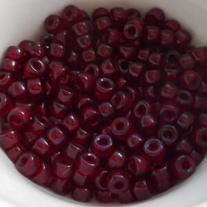 May include: A bowl filled with small, dark red glass beads. The beads are opaque and have a slight iridescent sheen.