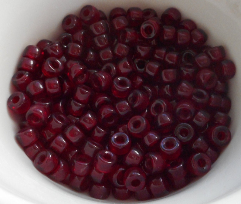 May include: A bowl filled with small, dark red glass beads. The beads are opaque and have a slight iridescent sheen.
