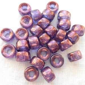 May include: A pile of purple glass beads with a metallic sheen. The beads are round with a hole in the center.