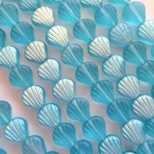 May include: A strand of light blue glass beads shaped like seashells with iridescent accents.