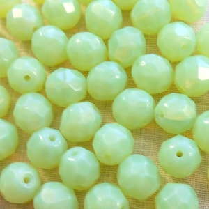 May include: A collection of light green faceted glass beads. The beads are round and have a smooth, polished finish.