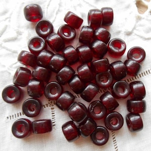 May include: A pile of dark red glass beads with a hole in the center of each bead. The beads are round and have a smooth, glossy finish.