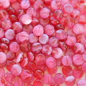 May include: A large group of pink and white glass beads. The beads are round and flat, with a slightly iridescent finish.