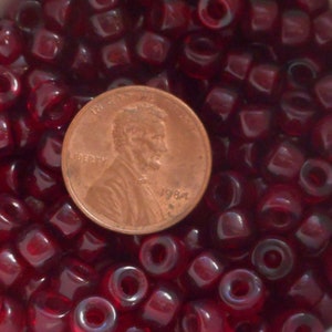 May include: A close-up image of a large quantity of small, dark red, glass beads. A US penny is included for scale.