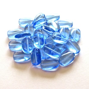 Zestaw 15 przezroczystych jasnoszafirowych, lekko skręconych, owalnych koralików ze szkła czeskiego - 14 mm x 8 mm, koraliki szklane prasowane C0032