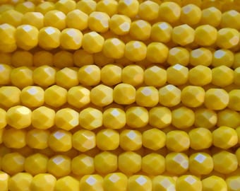 May include: A close-up of a strand of yellow faceted glass beads. The beads are round and have a shiny, iridescent finish.
