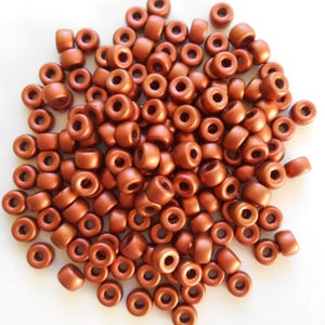 May include: A pile of small, round, copper-colored beads. The beads are smooth and have a metallic sheen.