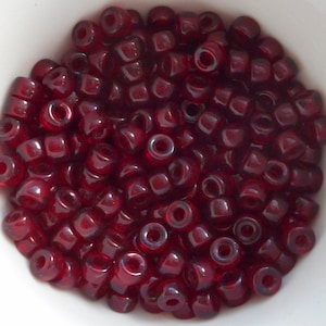 May include: A bowl filled with small, dark red, glass beads. The beads are round and have a slight shine to them.