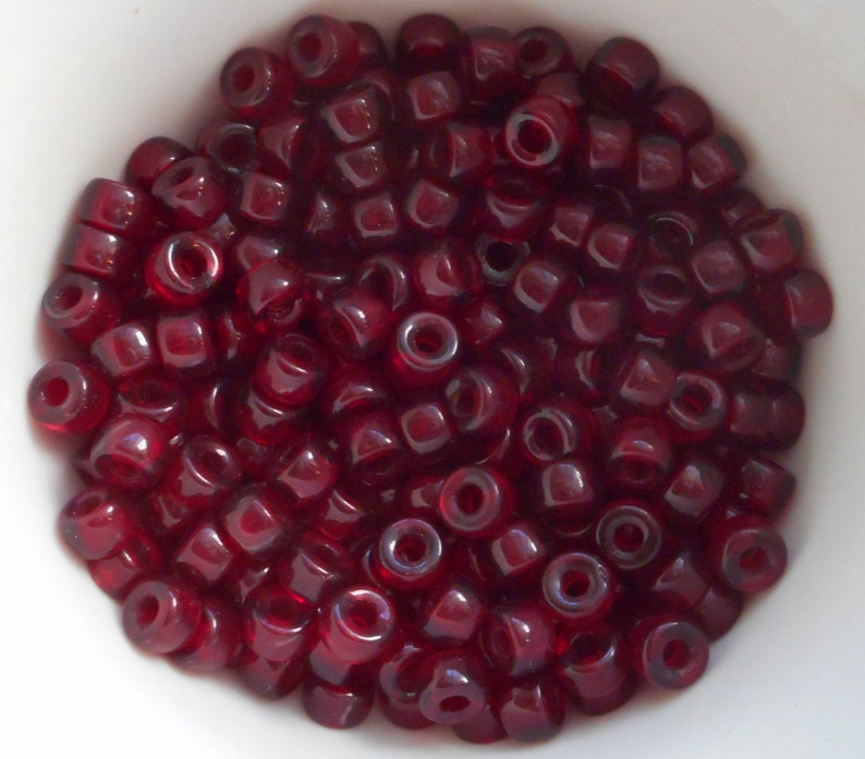 May include: A bowl filled with small, dark red, glass beads. The beads are round and have a slight shine to them.
