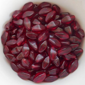 May include: A bowl filled with approximately 50 small, faceted, red glass beads. The beads are oval shaped and have a glossy finish.
