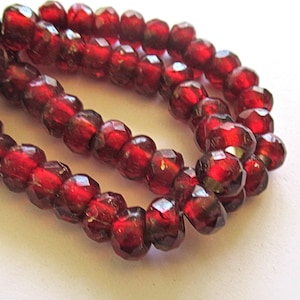 Può includere: Una collana di perline di vetro sfaccettate rosso scuro. Le perline sono rotonde e hanno una forma leggermente irregolare.