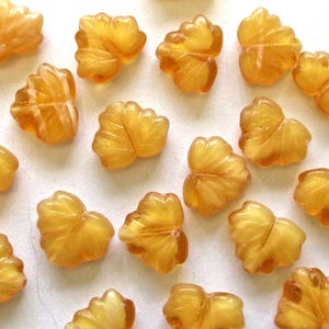 May include: A collection of amber glass leaf-shaped beads. The beads are translucent and have a slightly iridescent finish.