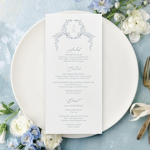 May include: A wedding menu card with a floral design and the initials "A N" at the top. The menu is on a white plate, with antique silverware tied with a ribbon. Blue and white flowers surround the plate, creating an elegant, romantic aesthetic.