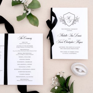 May include: Black and white wedding ceremony program with a black ribbon. The program lists the order of events for the ceremony, including the prelude, seating of the mothers, processional, bridal processional, words of welcome, opening prayer, statement of marriage, declaration of intent, exchange of vows, blessings and exchange of rings, scripture reading, closing prayer, presentation of the couple, and recessional. The program also includes the names of the bride and groom, Michelle Ann Dennis and Travis Christopher Haynes, and the date and location of the wedding, Saturday, the sixth of August, two thousand twenty-two, The Lodge at Torrey Pines, La Jolla, California.