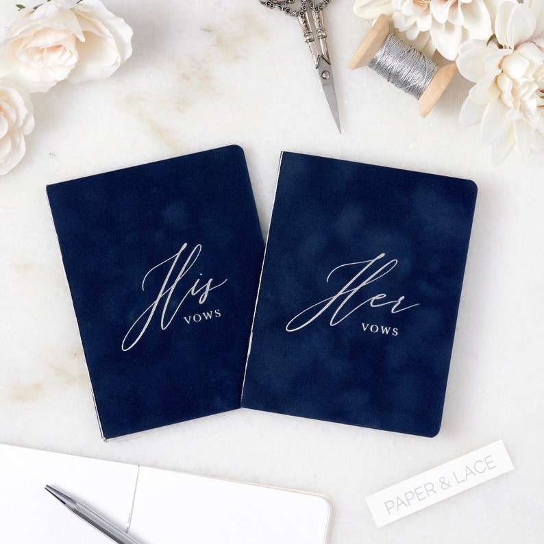 May include: Two navy blue velvet vow books with silver lettering. The book on the left says "His Vows" and the book on the right says "Her Vows".